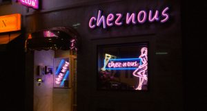 Eingangstür und Schaufenster des Nachclubs „Nacht Clubs“ in Köln, erleuchtet von pinken Neonlichtern, einer pinken Frauensilhouette, dem Namen in Leuchbuchstaben und einem gelben Champagnerglas